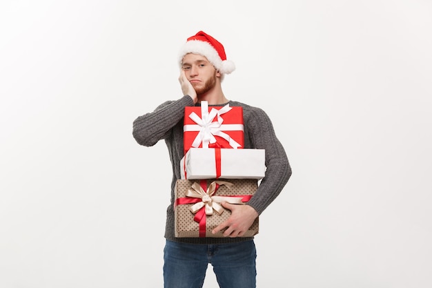 young handsome man with beard holding heavy presents with exhausted facial expression on white