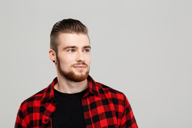 Giovane uomo bello con la barba che posa sopra la parete grigia.