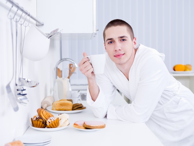 Giovane uomo bello con la tazza facendo colazione in cucina