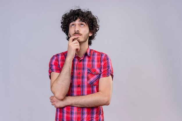 A young handsome man with curly hair in checked shirt looking up thinking 