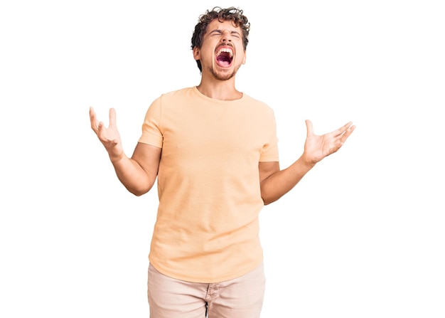 Free photo young handsome man with curly hair wearing casual clothes crazy and mad shouting and yelling with aggressive expression and arms raised frustration concept
