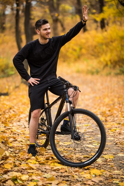 Young handsome man with his bike waving hello in autumn park