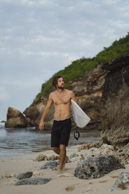 Young handsome man with a surfboard on a rock near the ocean.