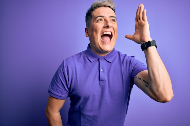 Бесплатное фото Молодой красивый современный мужчина в повседневной фиолетовой футболке на изолированном фоне громко кричит и кричит в сторону с рукой на рту концепция коммуникации