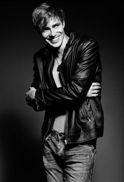 Young handsome muscled fit male model man in leather jacket posing in studio showing his abdominal muscles