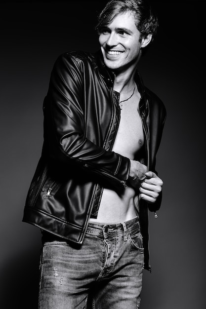 Young handsome muscled fit male model man in leather jacket posing in studio showing his abdominal muscles