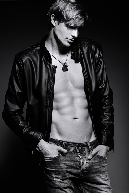 Young handsome muscled fit male model man in leather jacket posing in studio showing his abdominal muscles