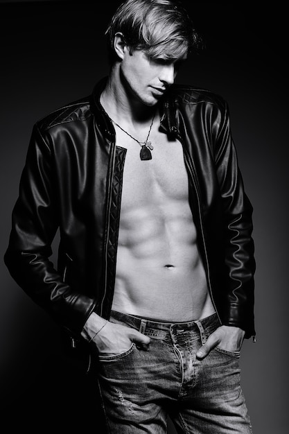 Young handsome muscled fit male model man in leather jacket posing in studio showing his abdominal muscles