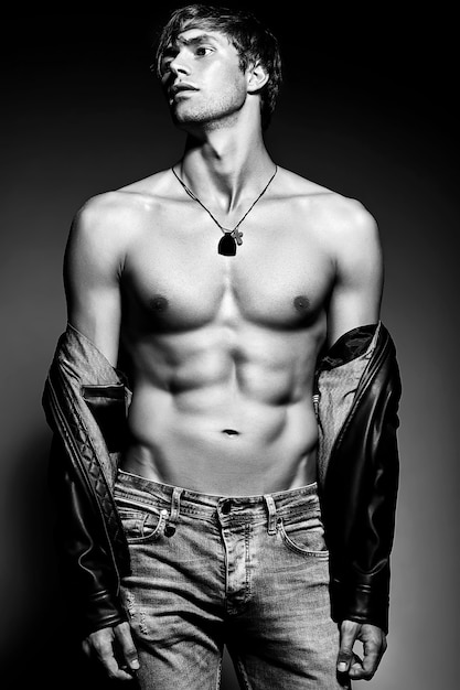 Young handsome muscled fit male model man posing in studio showing his abdominal muscles in  leather jacket