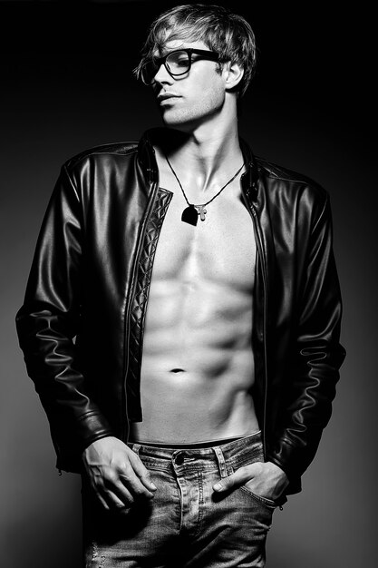 Young handsome muscled fit male model man posing in studio showing his abdominal muscles in  leather jacket