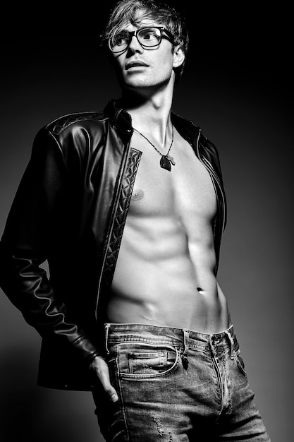 Young handsome muscled fit male model man posing in studio showing his abdominal muscles in leather jacket