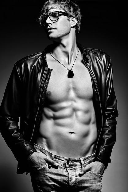 Young handsome muscled fit male model man posing in studio showing his abdominal muscles in leather jacket