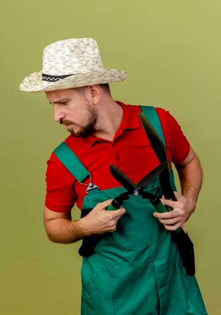 制服を着た若いハンサムなスラブの庭師と剪定ばさみを持って頭を左右に見下ろしている帽子