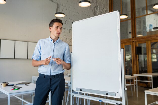 Young handsome smiling man standing at empty white board with marker