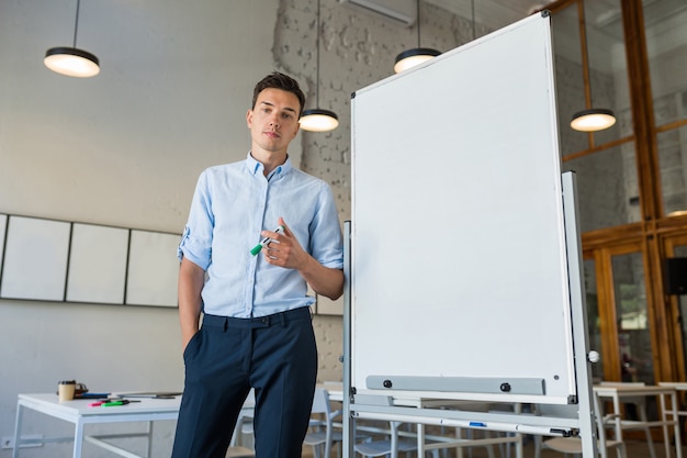 Young handsome smiling man standing at empty white board with marker