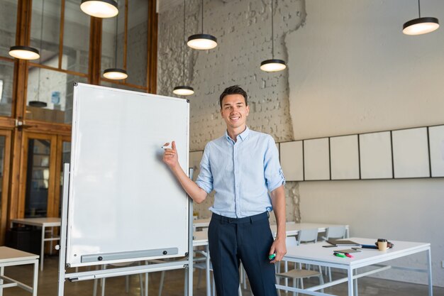 マーカーと空のホワイトボードに立っている若いハンサムな笑顔の男