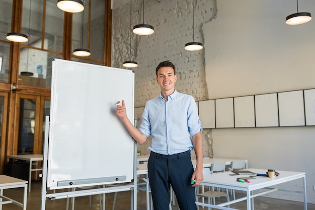 Young handsome smiling man standing at empty white board with marker