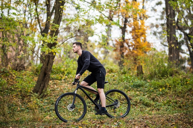 秋の時間に公園で彼の自転車のトレーニングを持つ若いハンサムなスポーツ男。