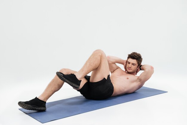 Молодой красивый спортсмен делает упражнения для ног на коврик для фитнеса