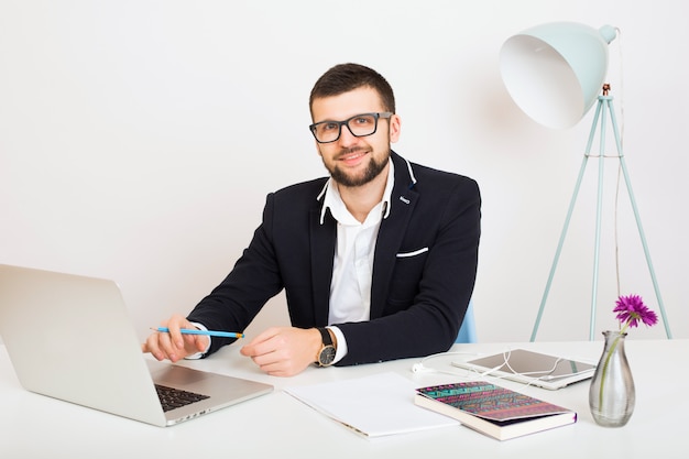 Young handsome stylish hipster man in black jacket working at office table, business style, white shirt, isolated, laptop, start up, work place, pencil, paper sheets, busy