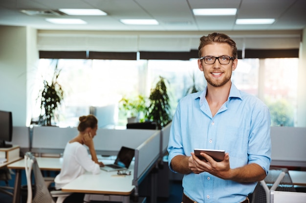 Foto gratuita giovane imprenditore di successo bello sorridente, tenendo tablet, sopra l'ufficio