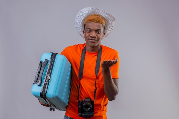 旅行スーツケースを持ってカメラとオレンジ色のtシャツを着て夏帽子の若いハンサムな旅行者少年