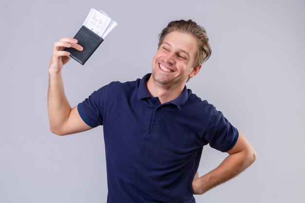 Young handsome traveler man holding air tickets happy and positive looking looking aside with confident smile on face standing over white background