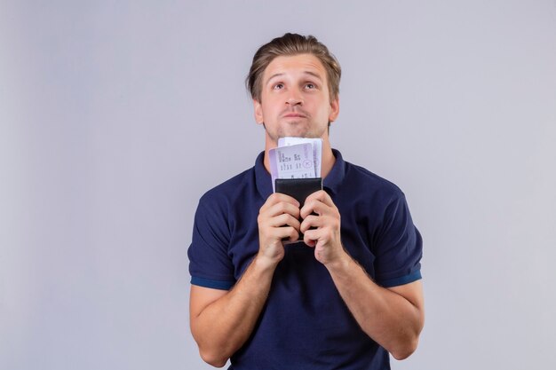 Young handsome traveler man holding air tickets looking up with dreamy look standing over white background