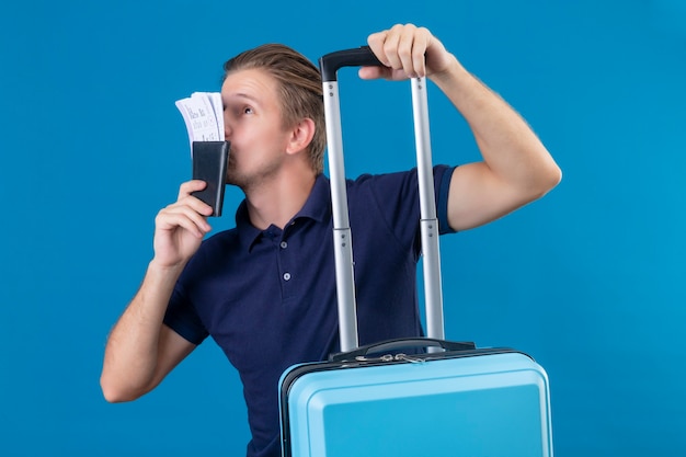 무료 사진 젊은 잘 생긴 여행자 남자 가방을 들고 파란색 배경 위에 행복 서 찾고 그의 손에 티켓을 키스