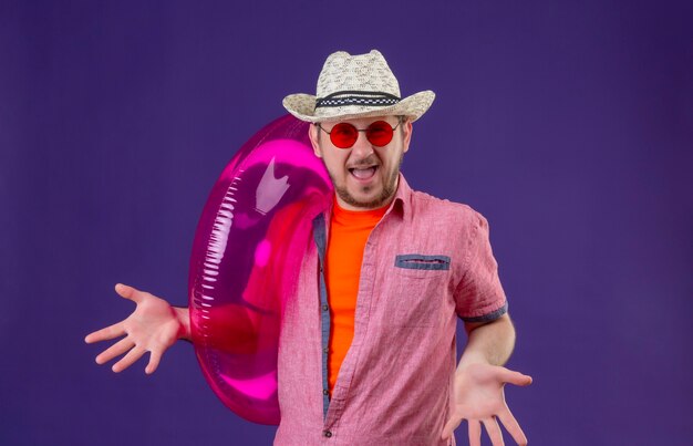 Free photo young handsome traveler man in summer hat with inflatable ring spreading arms