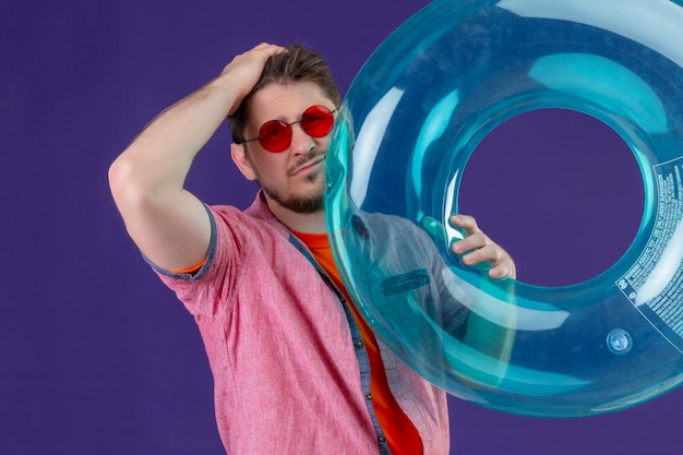 Young handsome traveler man with inflatable ring with hand on head for mistake