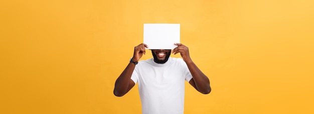 Free photo young happy africanamerican hiding behind a blank paper isolated on yellow background