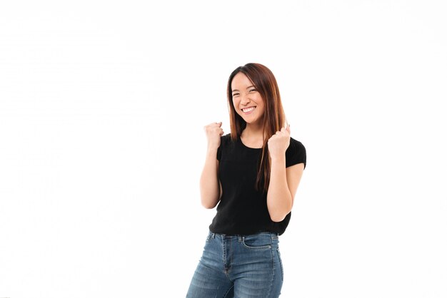 Молодая счастливая азиатская девушка в вскользь носке показывая жест победителя, смотря камеру