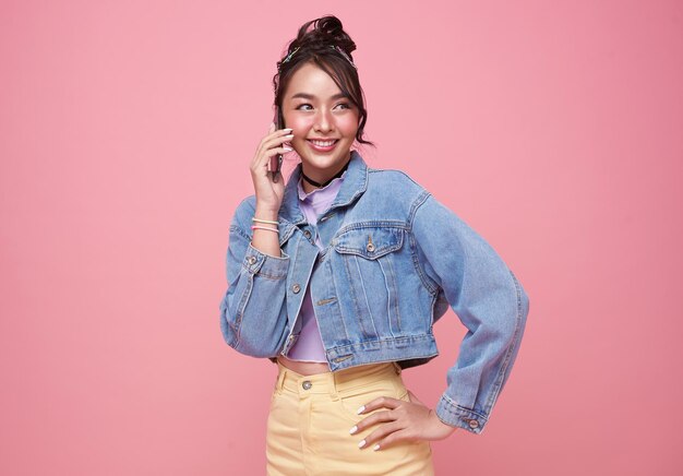 Young happy asian teen woman talking smart phone isolated over pink background.