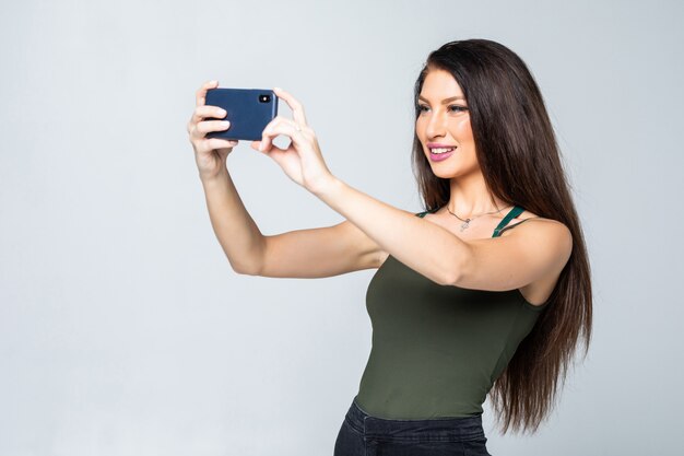 Young happy attractive female in dress takes photos using her mobile phone, shoot