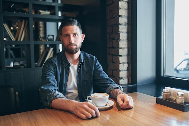 Young happy bearded man drinking morning fresh coffee. Caucasian handsome male business professional having coffee indoors.