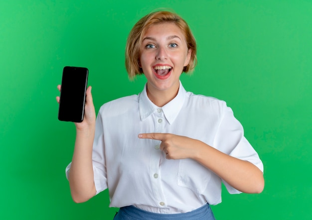 young happy blonde russian girl holds and points at phone