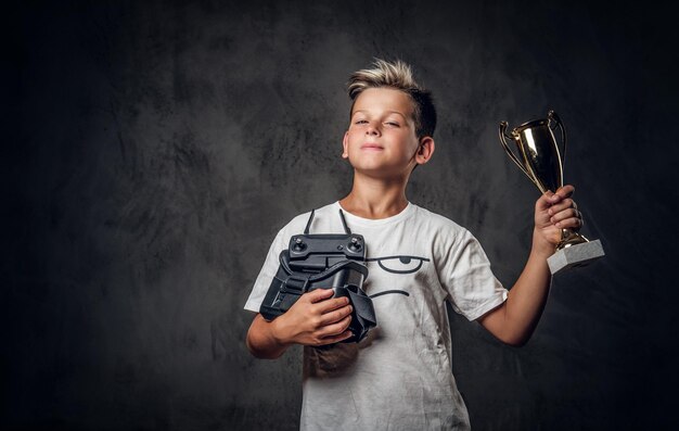 어린 행복한 소년은 가상 현실 게임에서 경쟁에서 이겼고 컵을 받았습니다.