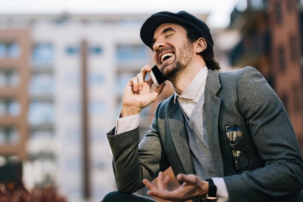 Young happy businessman having fun while communicating over mobile phone on the street