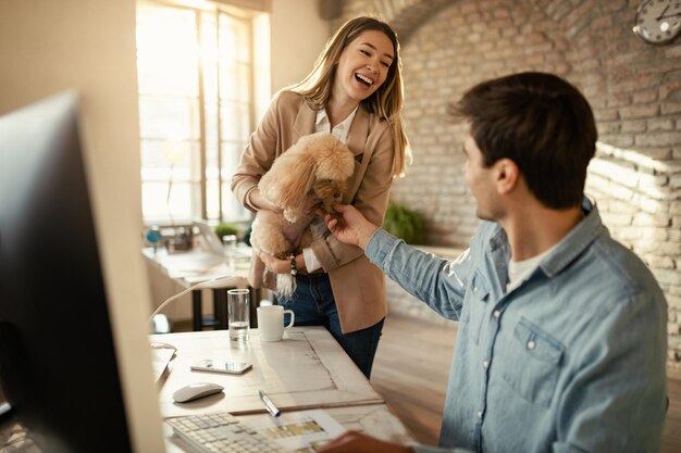 Молодая счастливая деловая женщина и ее коллега-мужчина развлекаются с собакой во время работы в офисе