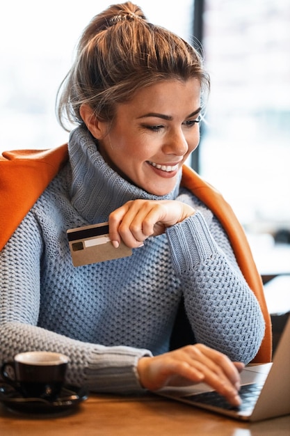 Free photo young happy businesswoman using credit card while surfing the net on laptop and shopping online