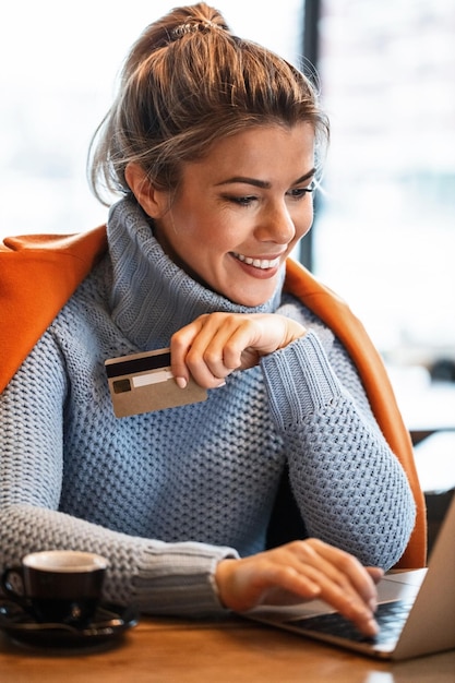 노트북으로 인터넷을 서핑하고 온라인 쇼핑을 하는 동안 신용 카드를 사용하는 젊은 행복한 여성