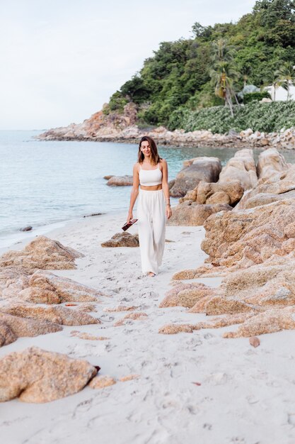 young happy calm caucasian woman with ukulele on tropical rocky beach at sunset