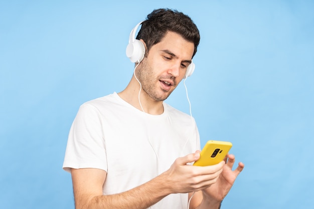 Молодой счастливый кавказский мужчина слушает музыку в наушниках у синей стены
