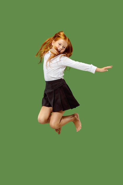 Young happy caucasian teen girl jumping in the air, isolated on green studio background. Beautiful female half-length portrait. Human emotions, facial expression concept.