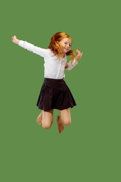Young happy caucasian teen girl jumping in the air, isolated on green studio background. Beautiful female half-length portrait.