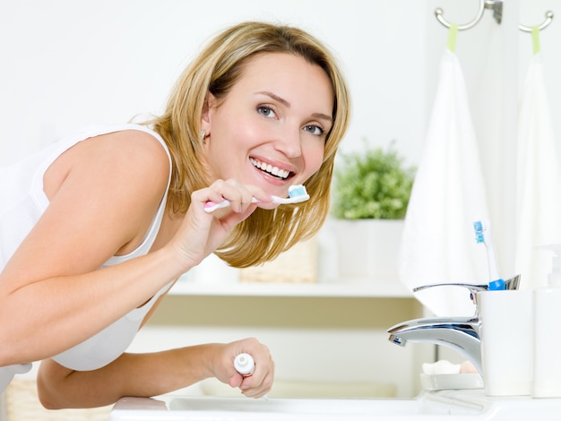 Giovane donna caucasica felice pulizia dei denti con spazzolino da denti in bagno