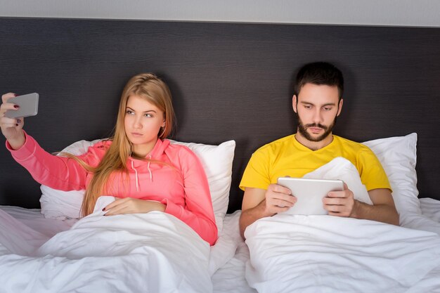 Young happy couple on bed  doing selfie with telephone camera. Concept about technology and people