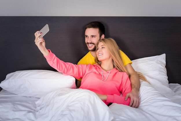 전화 카메라로 셀카를 하 고 침대에 젊은 행복 한 커플. 기술과 사람에 대한 개념