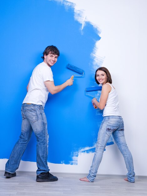 Молодая счастливая пара в повседневной одежде, чистящая стену